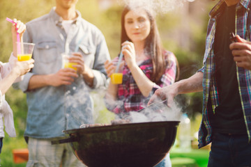 Company of friends spending time together frying meat. Group of friends cooking meat outdoors on grill on warm sunny day while on picnic.