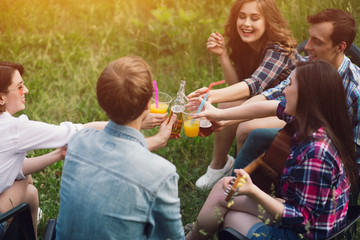 Obraz premium Happy friends sitting in park togetehr in circle. Two guys and three girls spending time together chilling in park on nice day outside with some drinks.