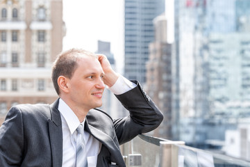 Young businessman closeup face portrait side profile of man standing in suit, tie, looking at New York City cityscape skyline in Manhattan at skyscrapers rooftop