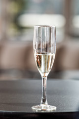 Macro closeup of one glass of white sparkling champagne wine in restaurant or wedding reception black table bokeh background, nobody