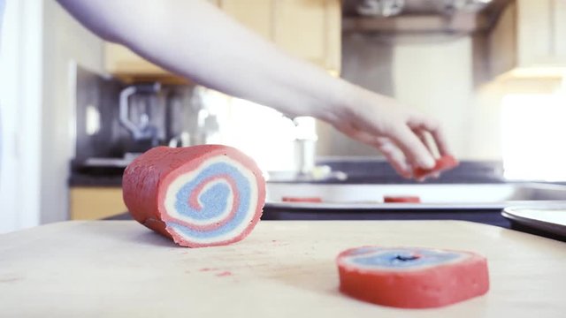 Slicing red white and blue pinwheel cookie dough into individual cookies