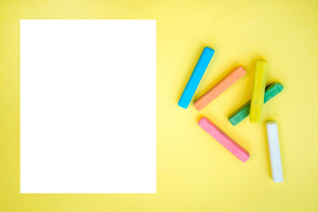 Colorful crayons and a sheet of white paper on a yellow background
