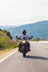 Young man riding a motorcycle on road in mountains in sunny day. 