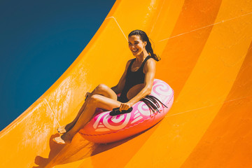 pretty brunette woman on the inflatable ring having fun on the orange water slide in the aqua park....