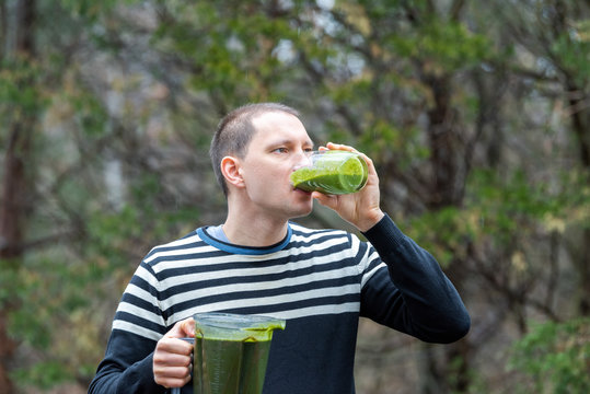 Young Man Standing Outside, Outdoors, Holding Plastic Blender Container, Drinking From Glass Green Smoothie Made From Vegetables, Greens