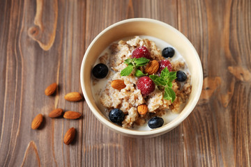 Oatmeal porridge in bowl topped with fresh blueberries and raspberries on wooden table. Top view.