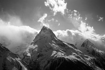 View on high mountains peak in sunlight clouds