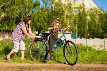 Obraz premium Grandmother teaches little granddaughter to ride old big bike
