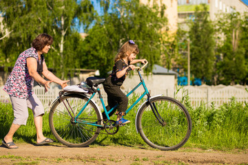 Grandmother teaches little granddaughter to ride old big bike