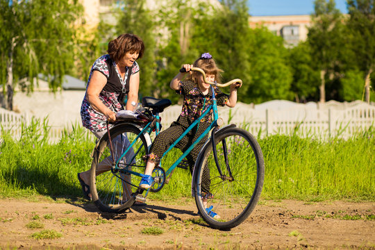 Grandmother teaches little granddaughter to ride old big bike