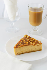 Slice of caramel cake with peanuts and a cup of coffee with cream