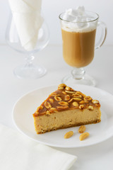Slice of caramel cake with peanuts and a cup of coffee with cream