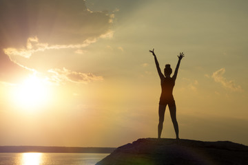 girl at the top of the mountain, raising her hands up against the sunset. Concept of sport, yoga, relaxation, meditation.