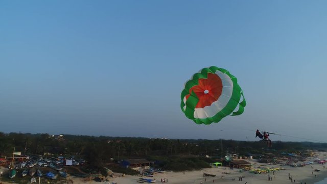 Take off and tow a multi-colored parachute from the beach over the sea at sunset. Aerial view.