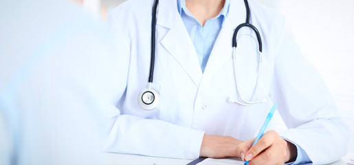 Unknown female doctor and patient discussing something while sitting at the table at hospital. Medicine and healthcare concepts