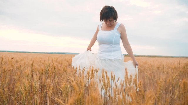 Plus size fashion model in slow motion video walking white dress on field wheat. fat woman on nature in the field grass lifestyle flowers summer. agriculture overweight female body. full girl length