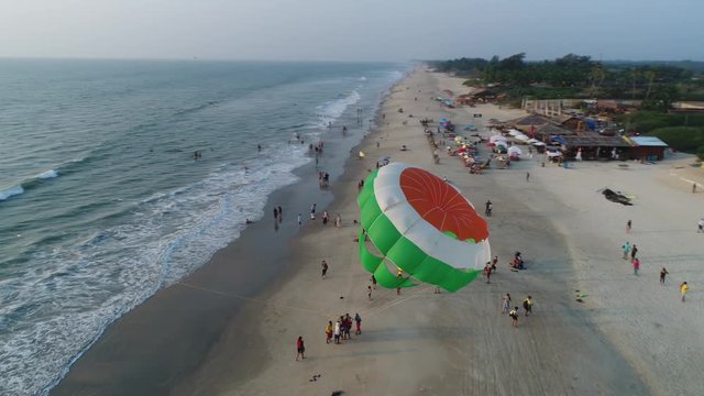 A colorful parachute lands on the beach and immediately flies up again. Extreme entertainment for tourists. Aerial view.