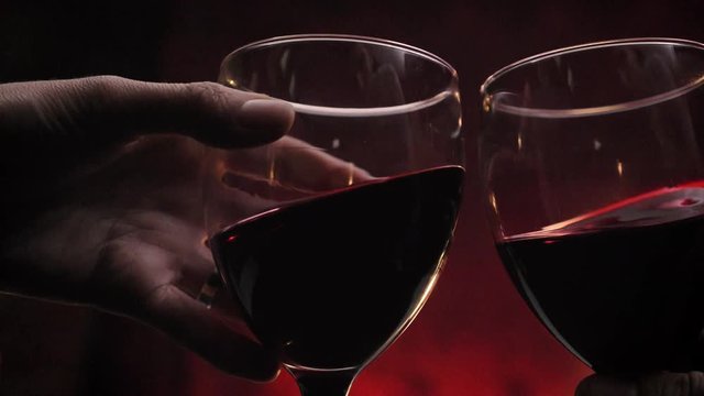 Hands holding two glasses of red wine during date, romantic dark red background, high quality video