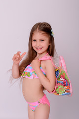 Naklejka premium Caucasian little girl in swimsuit with backpack and puzzle.