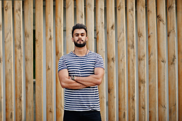 Handsome tall arabian beard man model at stripped shirt posed outdoor against wooden background. Fashionable arab guy.