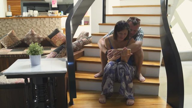 A man and a woman are sitting on the stairs in the house and watching movies on the smartphone