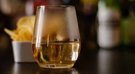 glass of whiskey with ice cubes and salty snacks on the background of bottles and bar