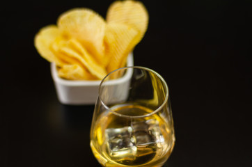 glass of whiskey with ice cubes and salty snacks on a black background