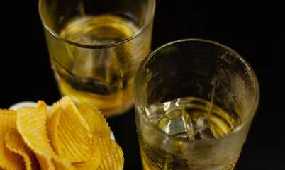 glass of whiskey with ice cubes and salty snacks on a black background