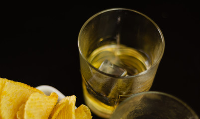 glass of whiskey with ice cubes and salty snacks on a black background