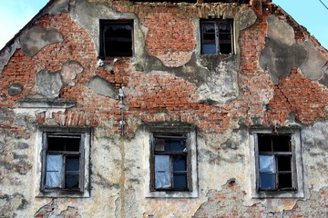 Fototapeta na wymiar Abandoned old ruined house closeup of broken walls with missing bricks, broken windows and fallen facade