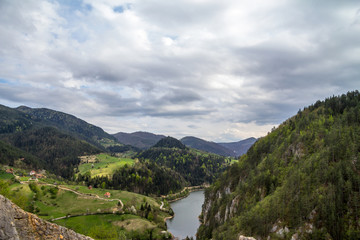 Zaovine valley and lake seen from the top of a cliff, with some mountain village houses seen, surrounded by pine trees, during a cloudy afternoon in Serbia, in the Balkans