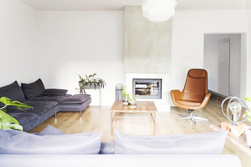 Stylish scandinavian interior with  design sofa, wooden table and fireplace. Bright and sunny room with plants and brown wooden floor.