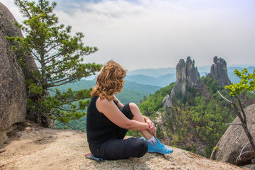 On a mountaintop/ Young female rock climber meditating on top of a mountain. In the background are...