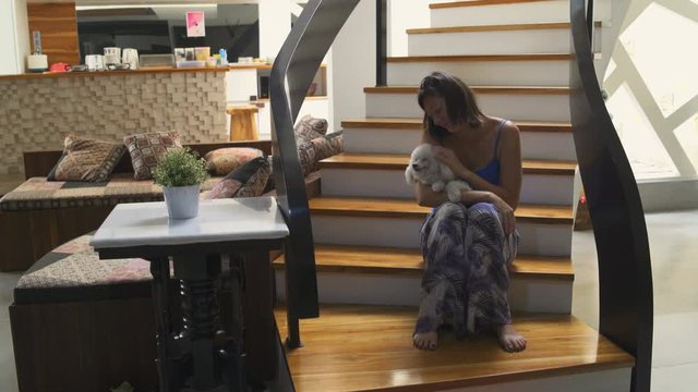 A woman sits on the stairs in the house with a small dog in her arms