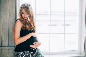 Beautiful young pregnant woman with long hair posing at home against window ..