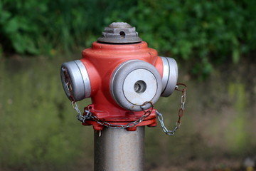 Metal red and grey fire hydrant top with four caps connected with small partially rusted chains on...