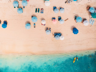 Top view of sandy beach with turquoise sea water and colorful blue umbrellas, aerial drone shot - obrazy, fototapety, plakaty