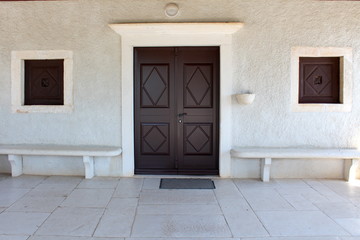 Massive new wooden chapel doors and windows on stone wall with stone benches and tiles in front