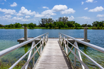 Ramp to boat dock on blue green lake with trees, vegetation and blue sky - Vista View Park, Davie, Florida, USA - obrazy, fototapety, plakaty