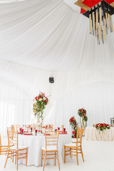 Beautiful banquet hall under a tent for a wedding reception. Interior of a wedding tent decoration ready for guests. Decor flowers. Red theme