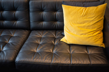 Yellow pillow on black leather couch closeup