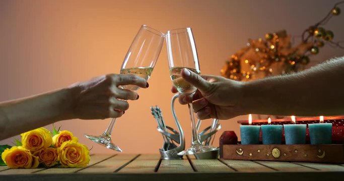 Couple tinkles glasses. Two glasses of champagne, candles on the wooden table. Cheers. Romantic evening.