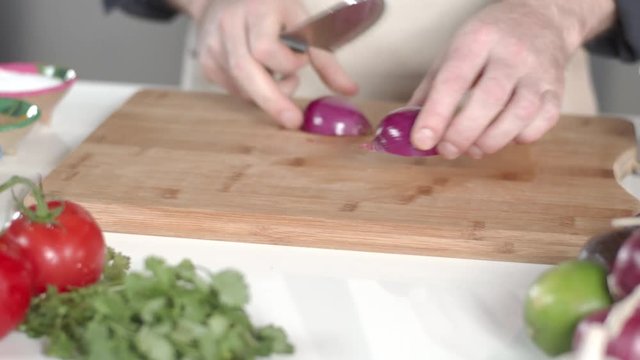 Slow-mo tracking shot of chef slicing red onion with large kitchen knife