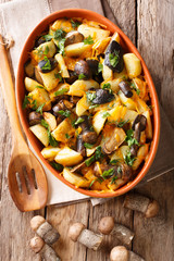 Fried potatoes with boletus mushrooms, cheddar cheese and herbs close-up in a platter. Vertical top view