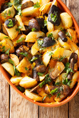 Baked potato wedges with forest mushrooms, cheddar cheese and herbs close-up in a baking dish. Vertical top view