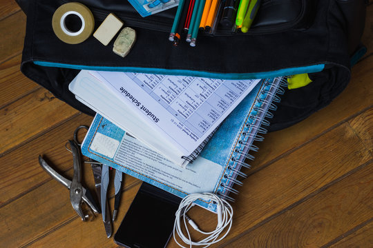 Regreso a clases con la mochila llena de libretas y accesorios como plumas, tijeras, aud&iacute;fonos, horario de clases, sobre un fondo de madera