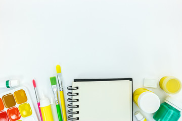 school supplies with a notebook, paints, brushes on white desk background, flat view