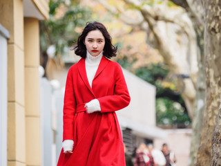 Beautiful young brunette woman wearing a red coat in autumn city. Outdoor fashion portrait of glamour young Chinese cheerful stylish lady in street. Emotions, people, beauty and lifestyle concept.