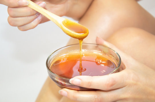 The girl is holding a bowl with a wooden spoon in her hands. With liquid sugar, for epilation. With liquid honey. Close-up.