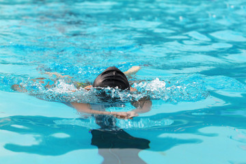 Young swimmer with black swimming cap swims breaststroke in the swimming pool for competition